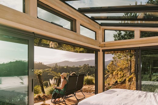 Two people sit on a deck and look out over an incredible view of the Karangahake Gorge.