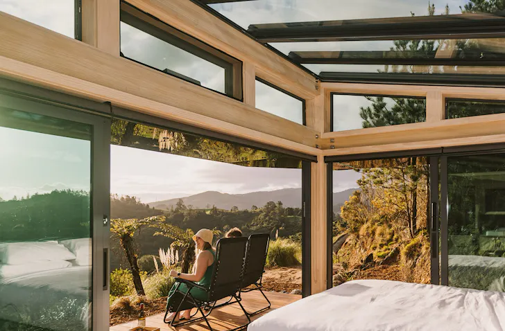 Two people sit on a deck and look out over an incredible view of the Karangahake Gorge. 