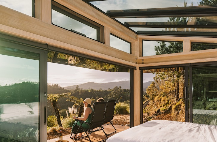 Two people sit on a deck and look out over an incredible view of the Karangahake Gorge. 