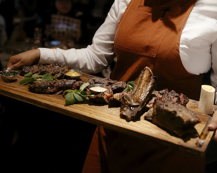 A waitress carries a massive slab of meat on a wooden board.