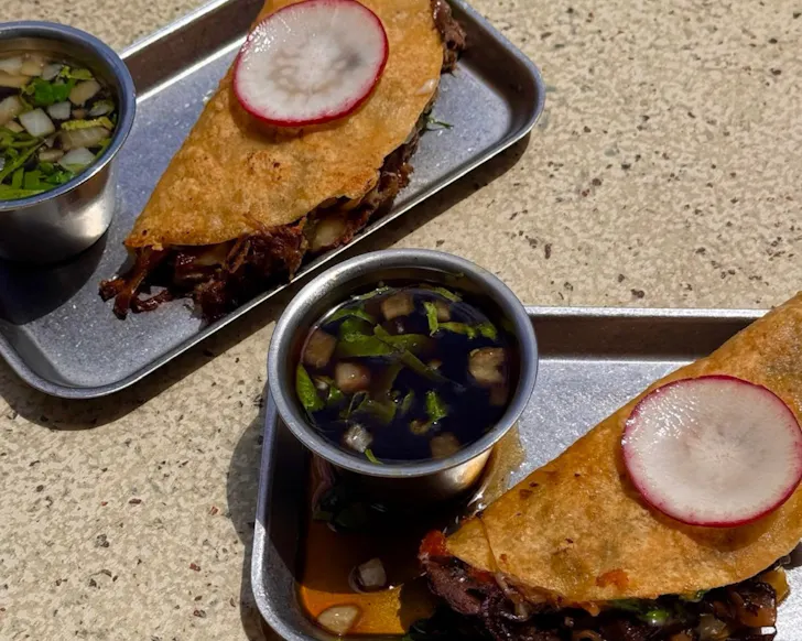 Two tacos on plates with dipping sauce