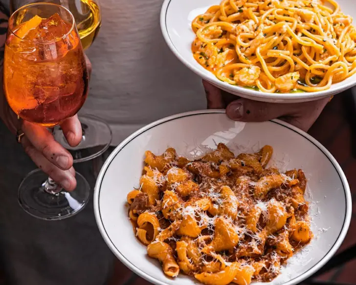 Two plates of pasta and aperol in hands
