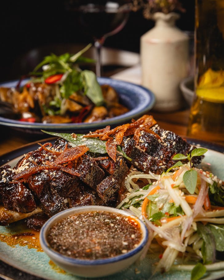 A plate of beef ribs with a side of papaya and apple salad and Thai dipping sauce