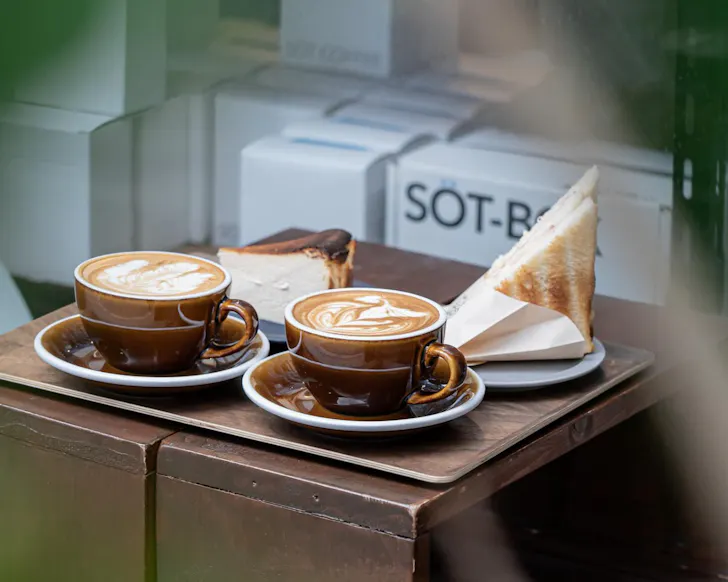 Two cups of large milk coffees at SOT Coffee Roasters, served with basque cheesecake and a sandwich.
