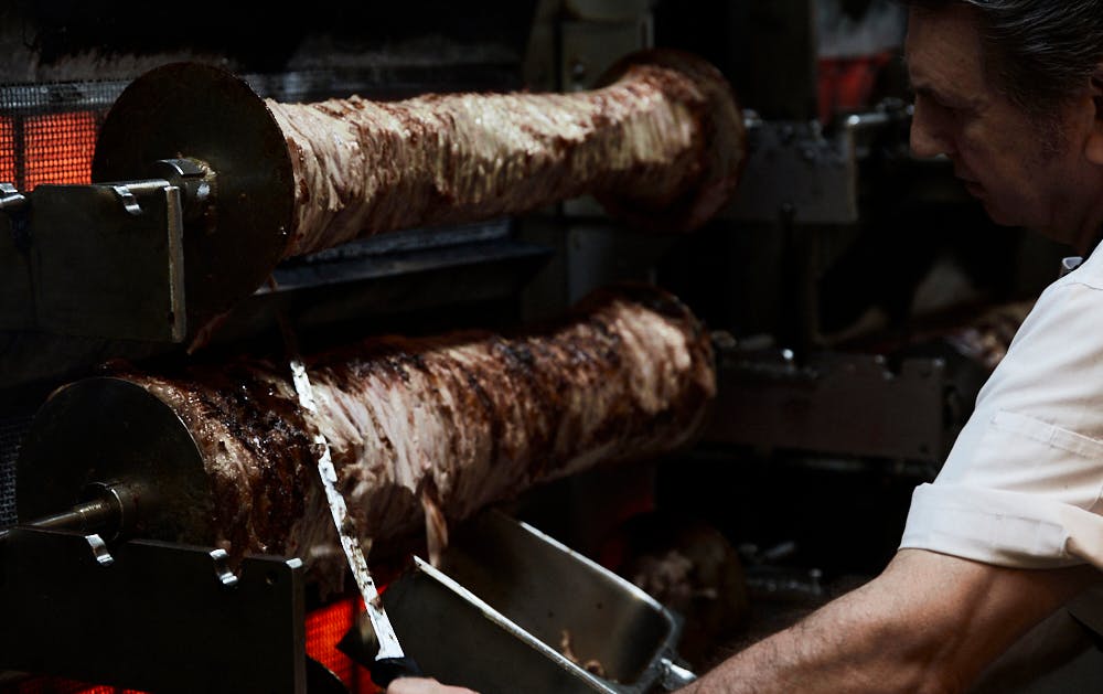 A man carving meat off in a kitchen.