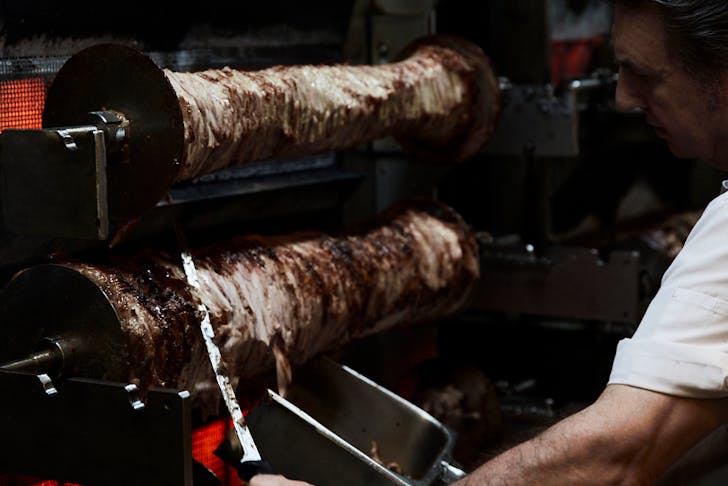 A man carving meat off in a kitchen.