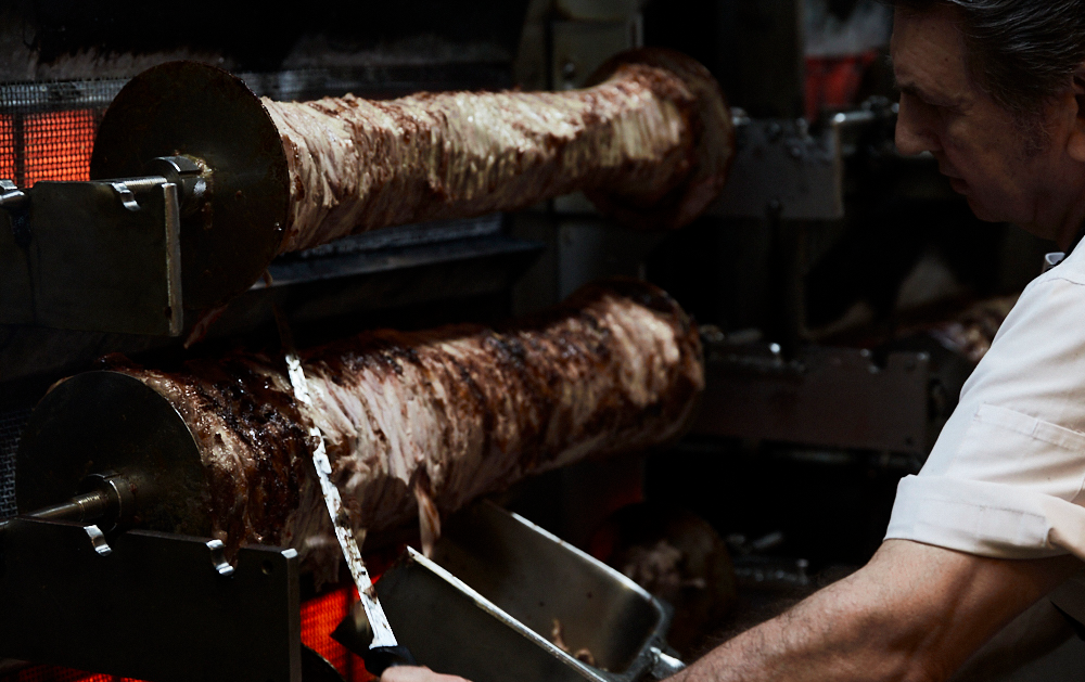 A man carving meat off in a kitchen.