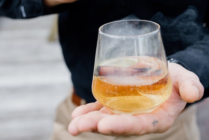 someone holding a glass of smoking whiskey in their palm