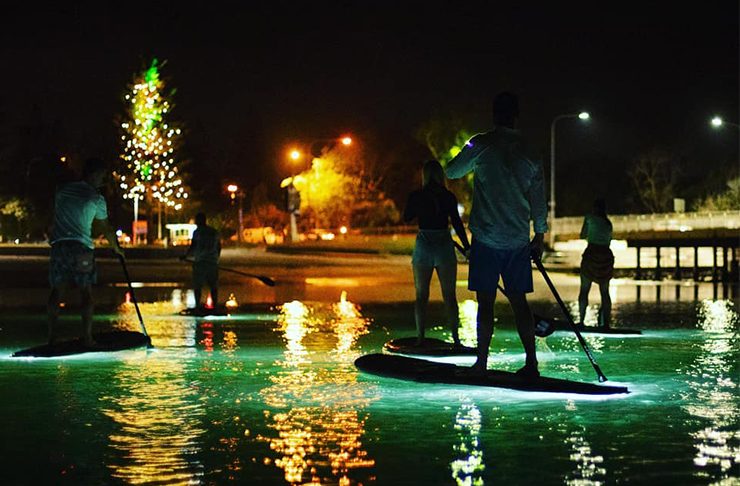 people paddle boarding on glowing paddle boards in the dark