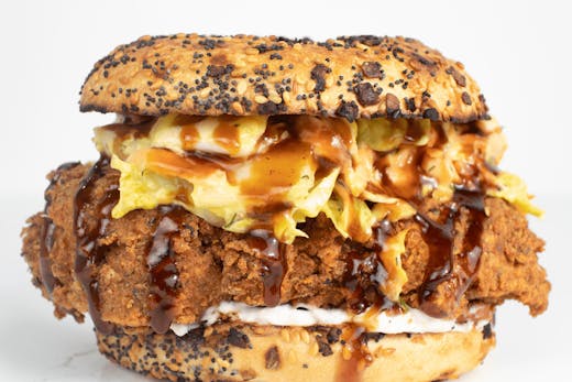 a fried chicken bagel with sauce dripping out.
