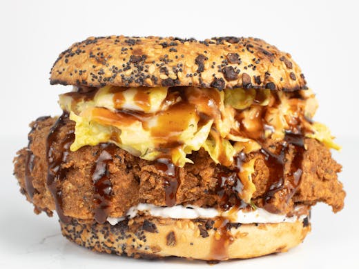 a fried chicken bagel with sauce dripping out. 