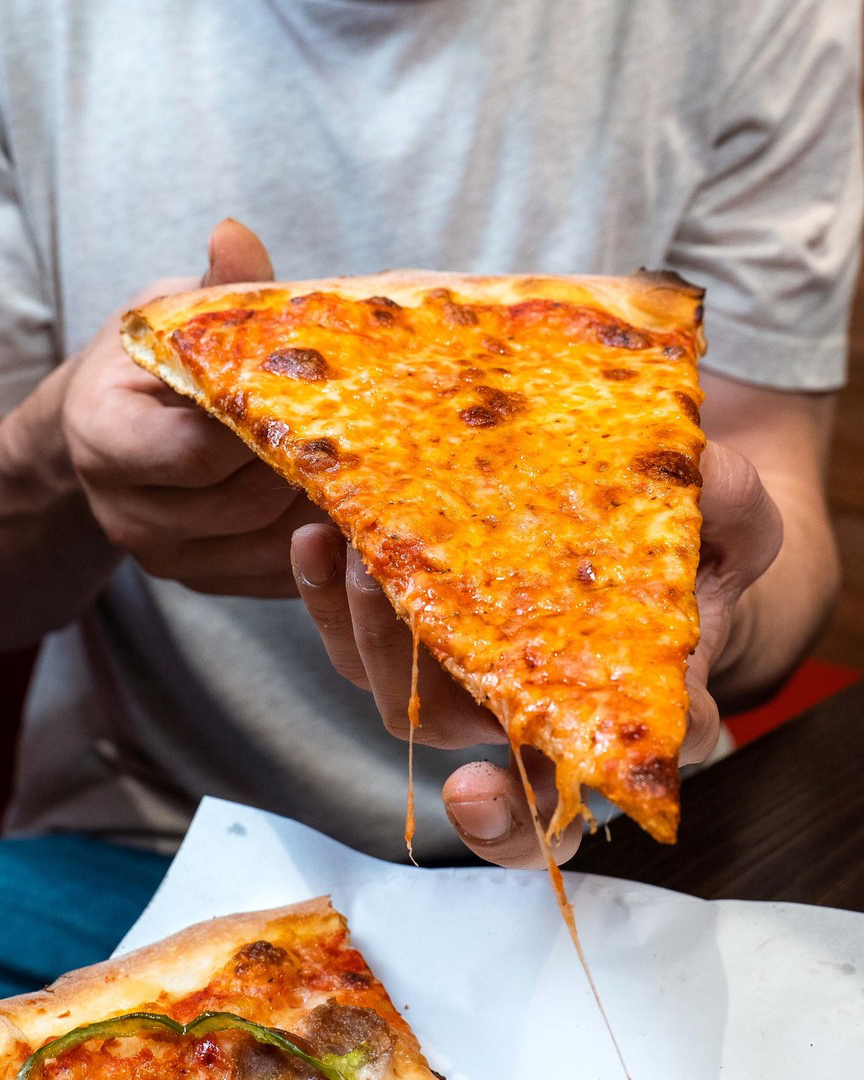 A person holding up a large NYC-style pizza slice, a cheap restaurant Melbourne.
