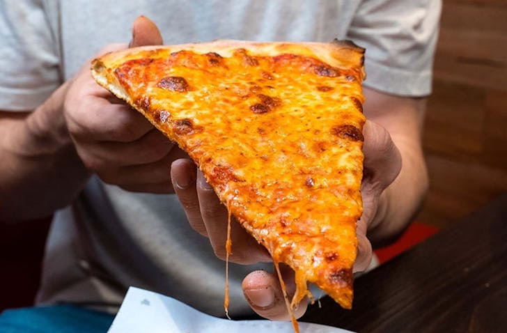 A person holding a large pizza slice at a best late-night eats Melbourne spot. 