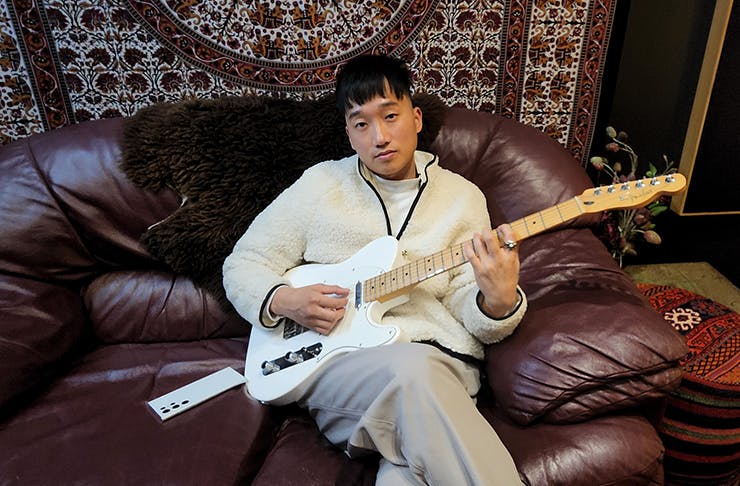 Music Artist Taebz sitting on a couch holding a guitar looking at the camera.