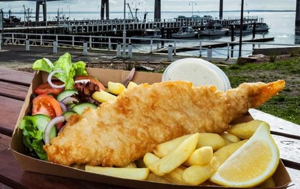 A tray of fish and chips with a large pier in the background. 