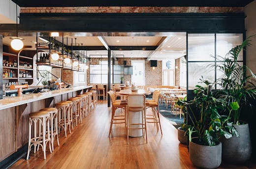 The interior of the pub with wooden floors a long bar and plants.