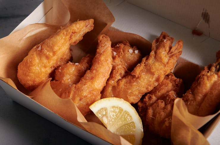 A box full of crunchy golden friend fish with a wedge of lemon. 