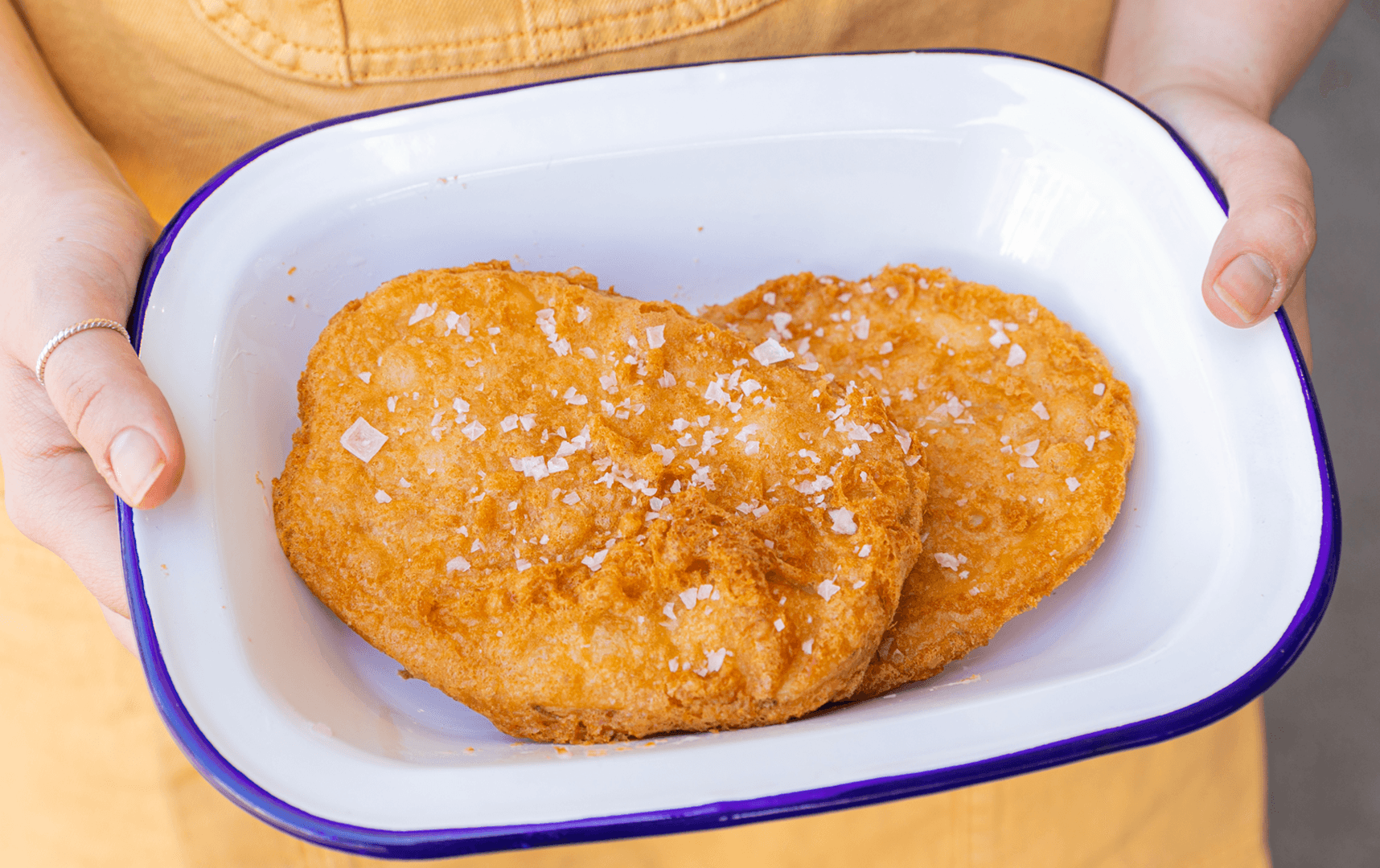 A person holding a tray with large potato cakes at a fish and chips Melbourne shop.