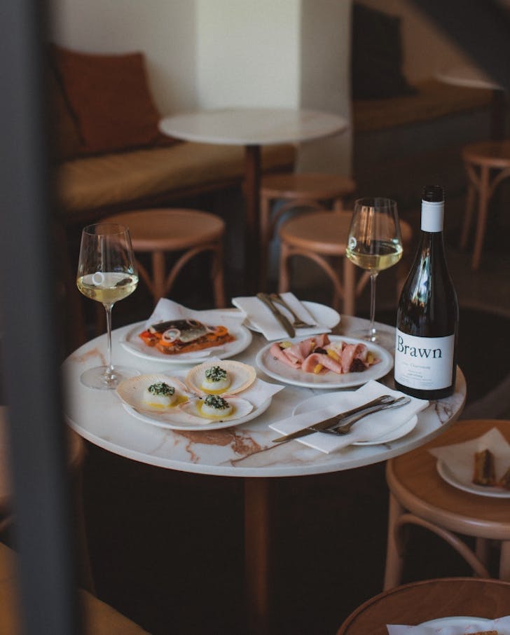 A cosy table for two inside at Vinotto, with multiple share plates, a bottle of white wine and two glasses 