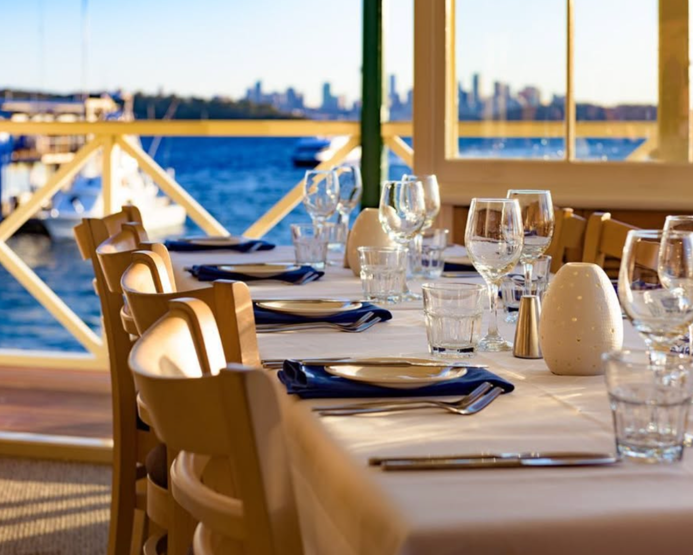 Side view of a dining table inside Doyles restaurant. In the background is a view through an open door, featuring the water and Sydney's skyline