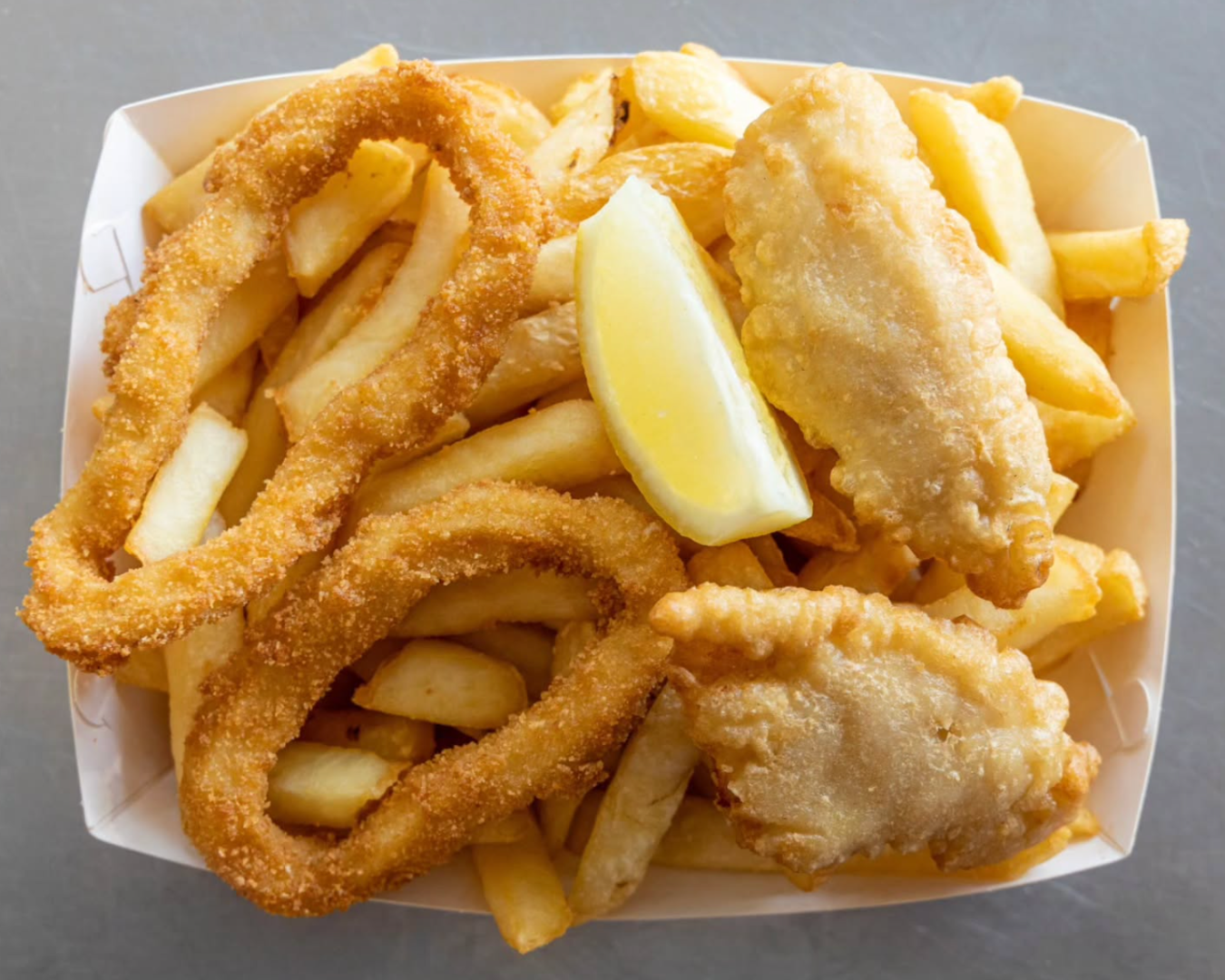 Above view of a box of fish and chips, with calamari and fish pieces included.