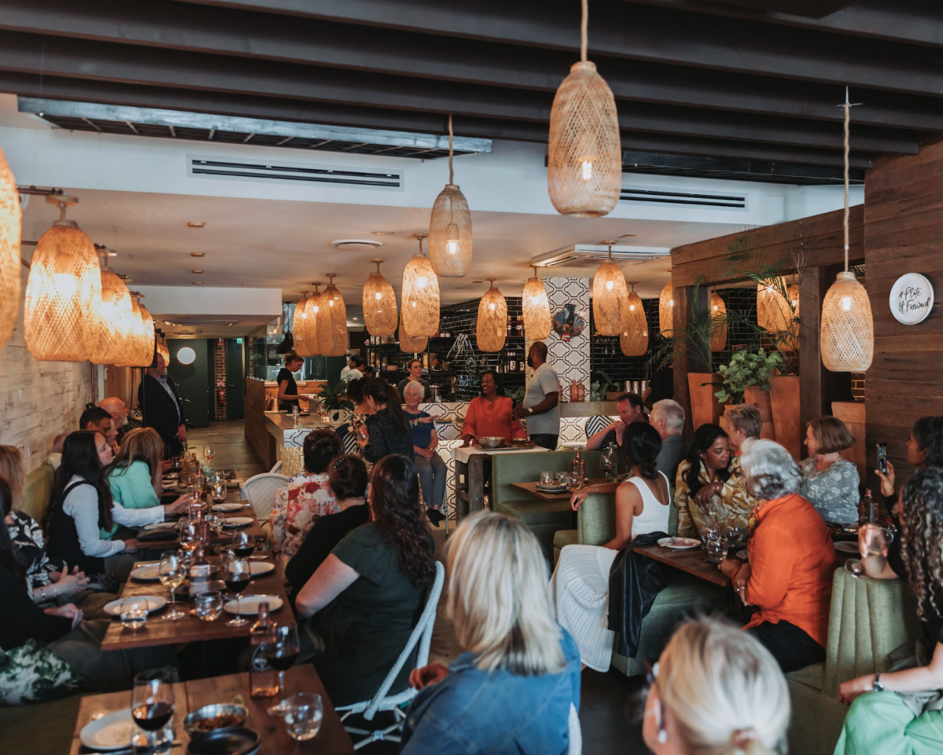 A wide shot of an indoor restaurant packed with people sitting and laughing at dinner tables. The mood is light and pleasant.
