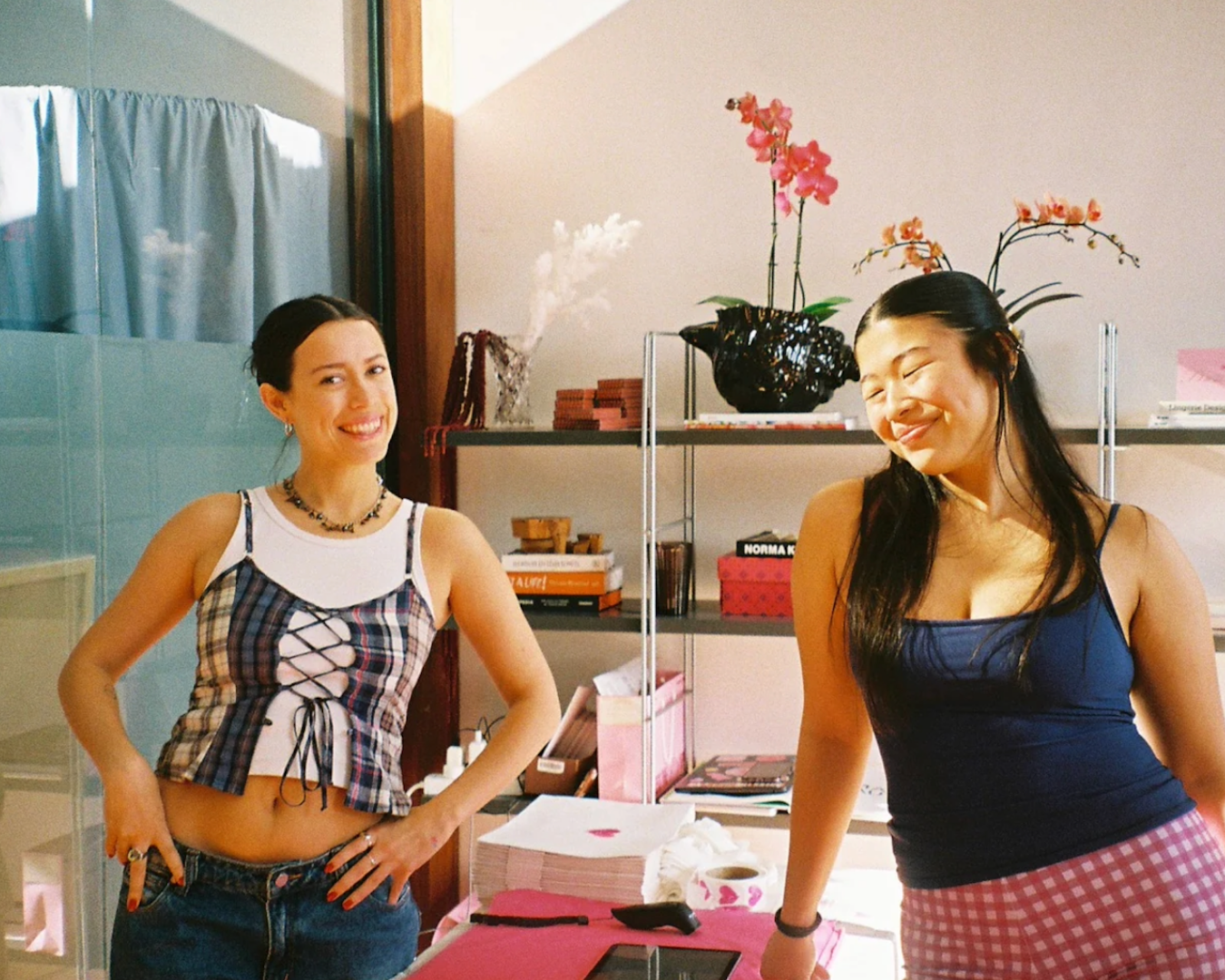 A mid shot of two girls inside the Katherina Lou studio wearing the clothing pieces of the brand and smiling at the camera.