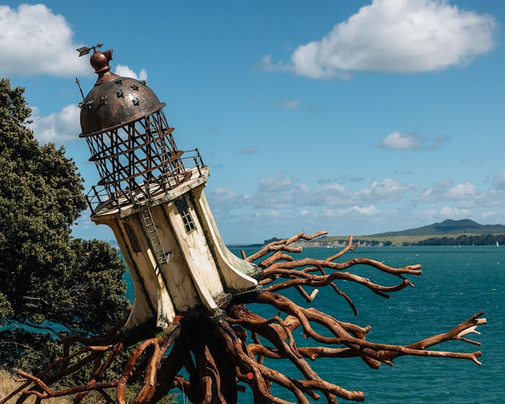 A lighthouse sculpture attached to tree roots, jutting out over the ocean. 
