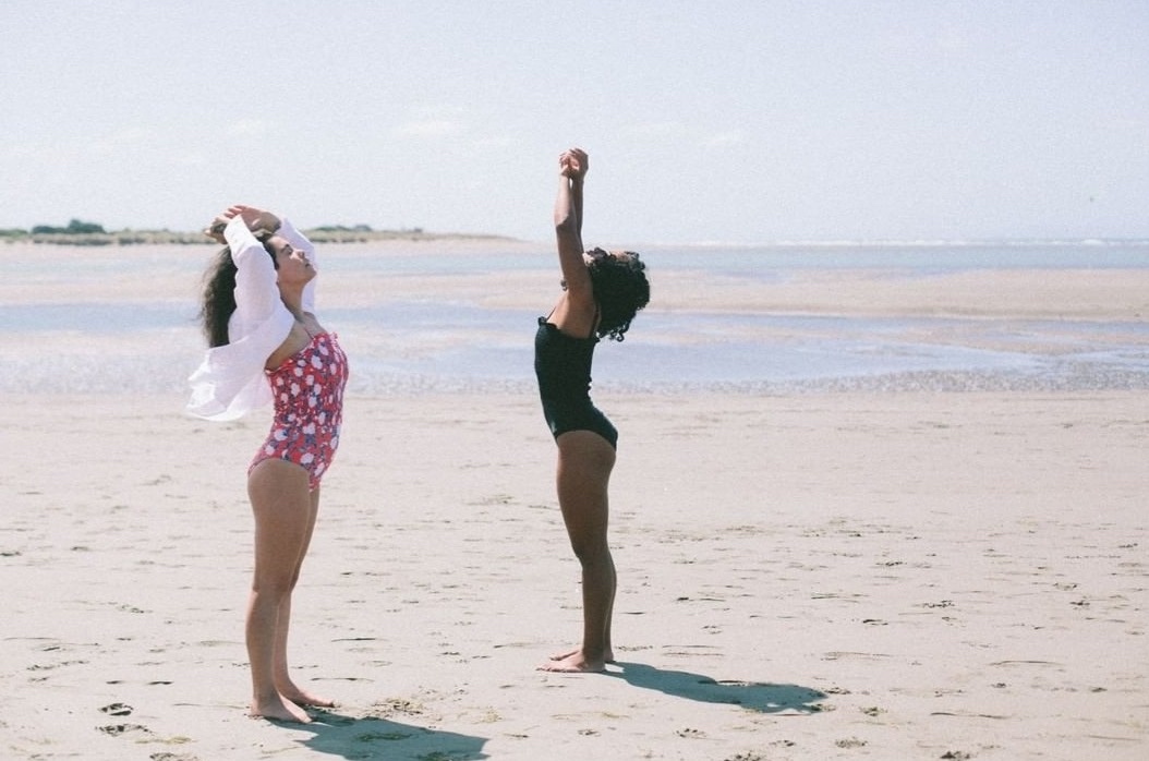 Two women with their arms up to the air take a moment to breathe while being on the beach.  
