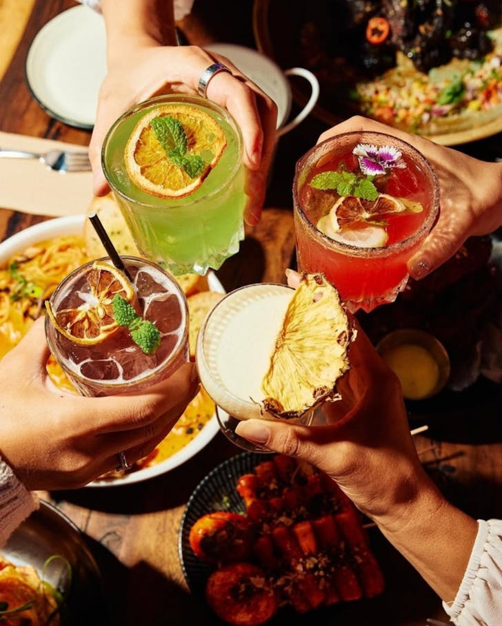 Four hands holding brightly coloured soju cocktails in cheers.