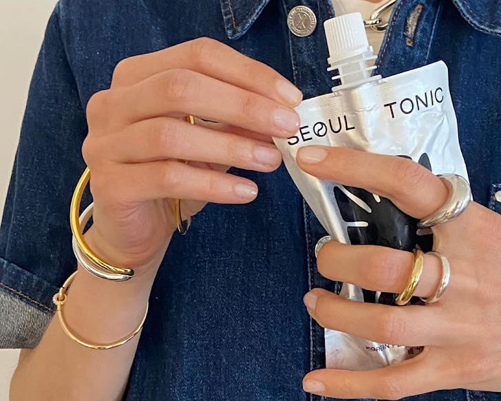 Someone wiht lots of gold and silver rings squeezes a packed of Seoul Tonic. 