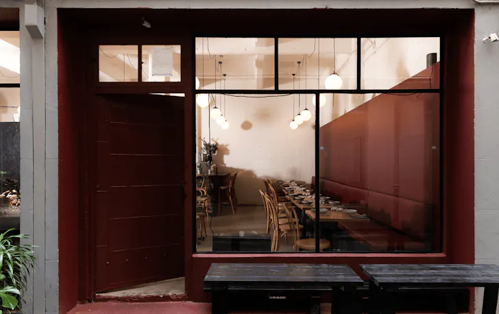 The front of a restaurant with a door ajar and the lights on inside. 