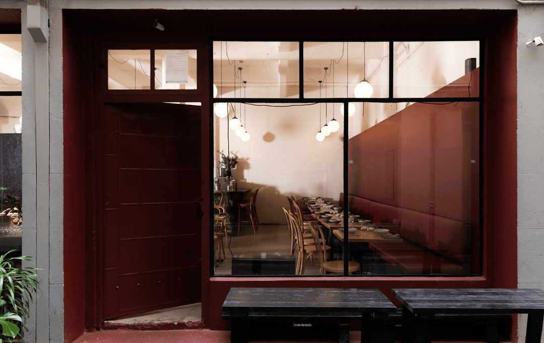 The front of a restaurant with a door ajar and the lights on inside. 