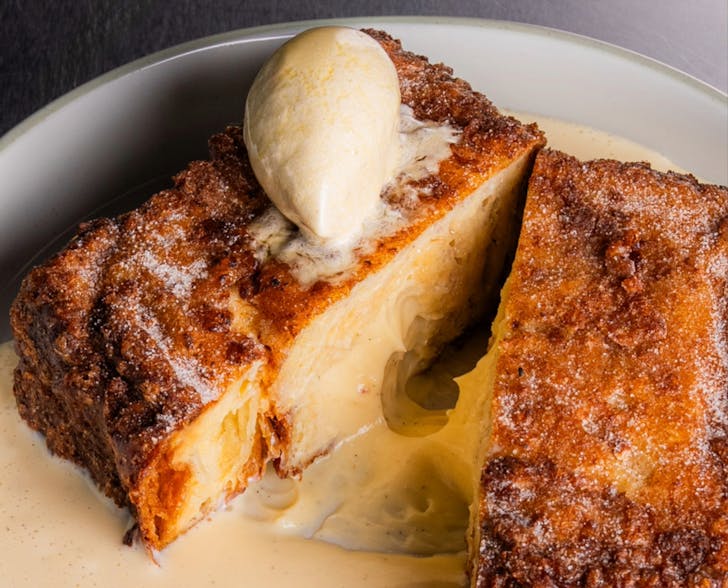 A close up photo of Shadow Bakings croissant loaf French toast, split in the middle. The split reveals soft fluffy pastry inside with creamy sauce.