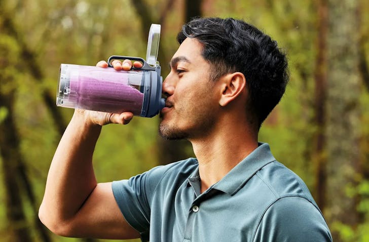 A man sips from the Ninja Blast Max Cordless Portable Blender while out and about