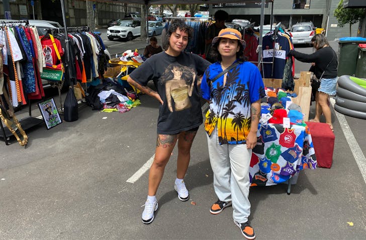 Sian and Tina stand in front of a clothing pop up store with racks upon racks of vintage clothing