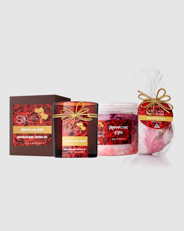 A soy candle in a dark red glass, a tub of pink and white bath salts and a pink and white bath bomb.
