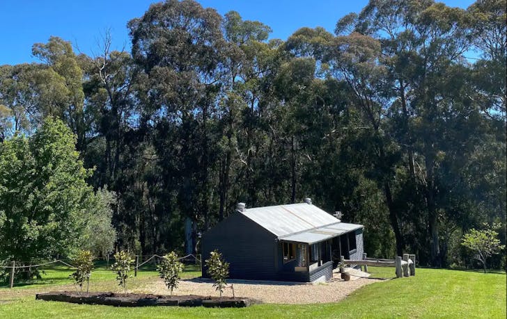 A cottage set against the blue sky and trees, a best dandenong ranges accomodation option.