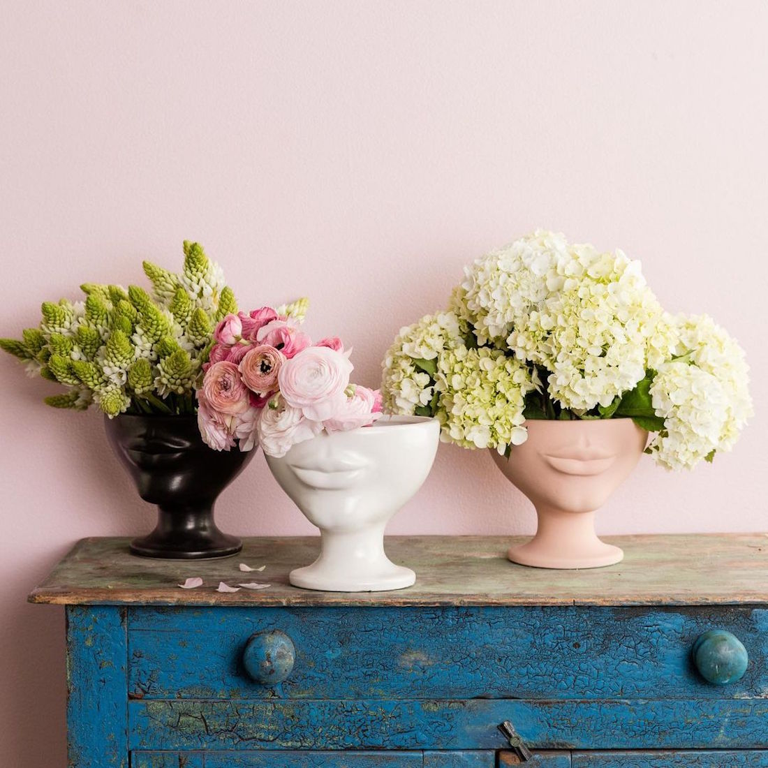 Three vases sit on a rustic hallway table with blooms overflowing.