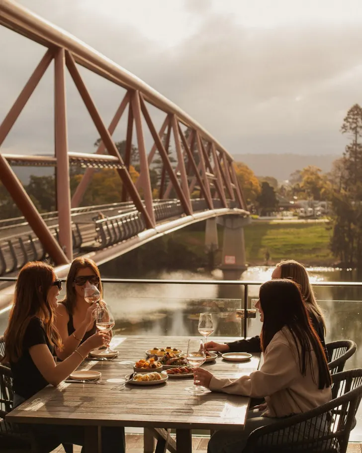 A group of friends sit outside on the deck at Sinclair's over the Nepean River.