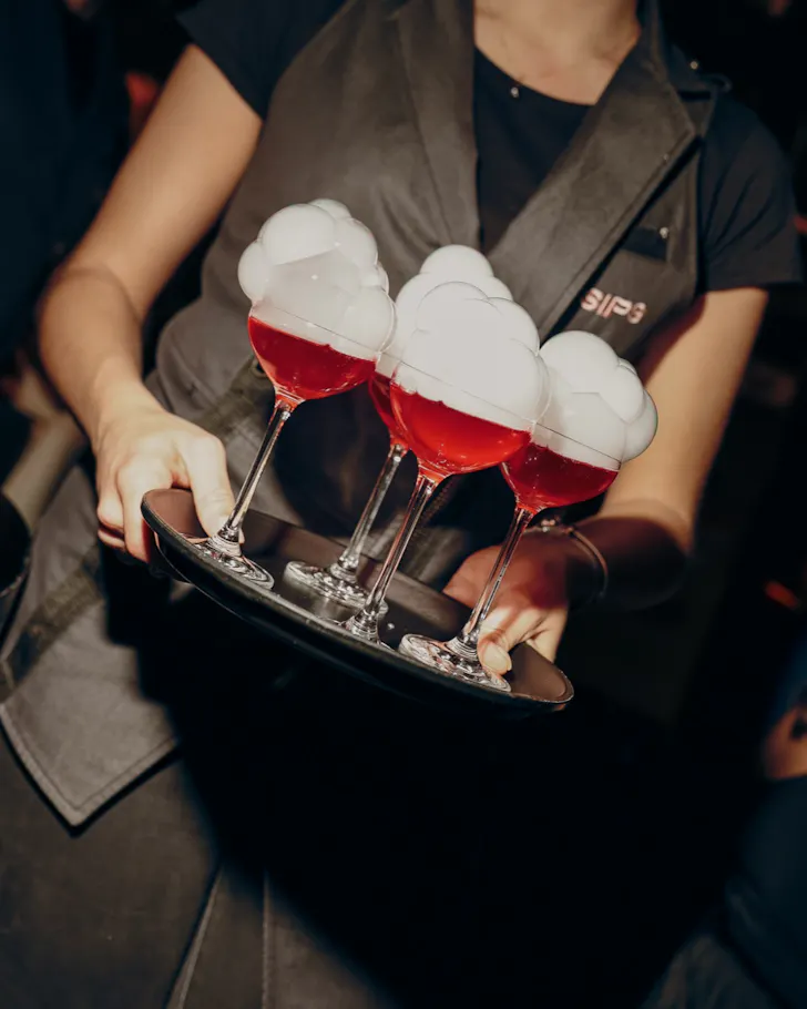 A waiter carrying a round of fun, red cocktails with white foam at SIPS, Barcelona.