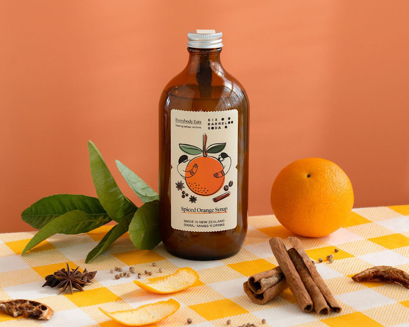A bottle of limited edition Spiced Orange Soda sits on a table with orange rind, leaves and cinnamon sticks. 