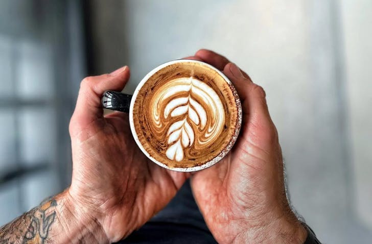 Man with tattoos holding coffee.