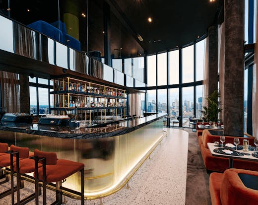 A large bar in the centre of a room with a large window overlooking the city.