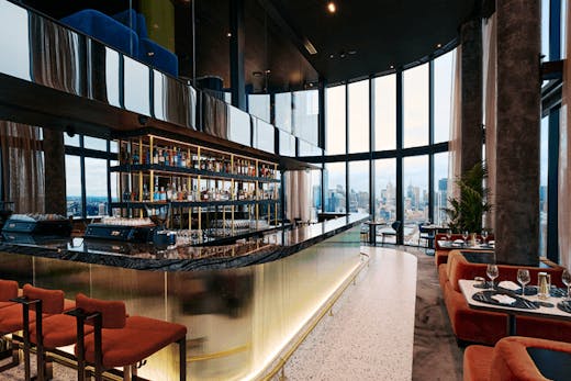 A large bar in the centre of a room with a large window overlooking the city.