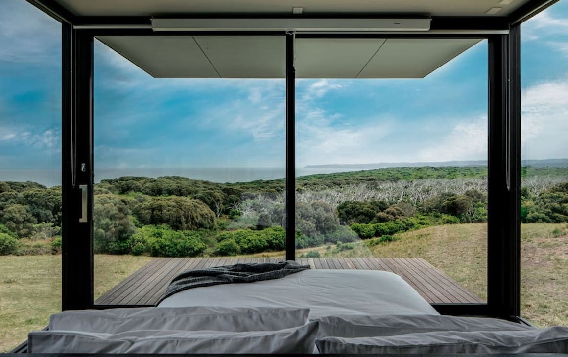 A bed with glass walls overlooking a large range at one of the best romantic getaways in Victoria.