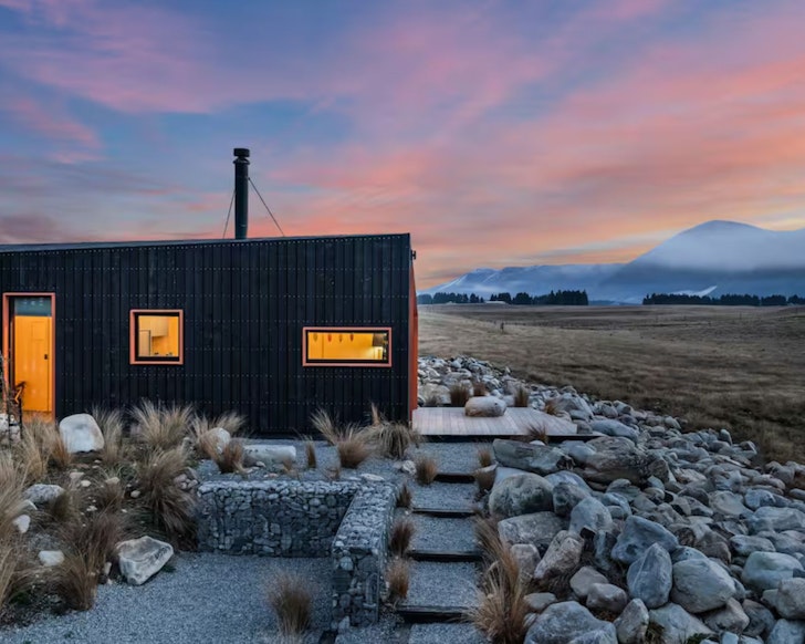The sleek black lines of Skylark Cabin surrounded by mountains. It's one of the best romantic stays in New Zealand