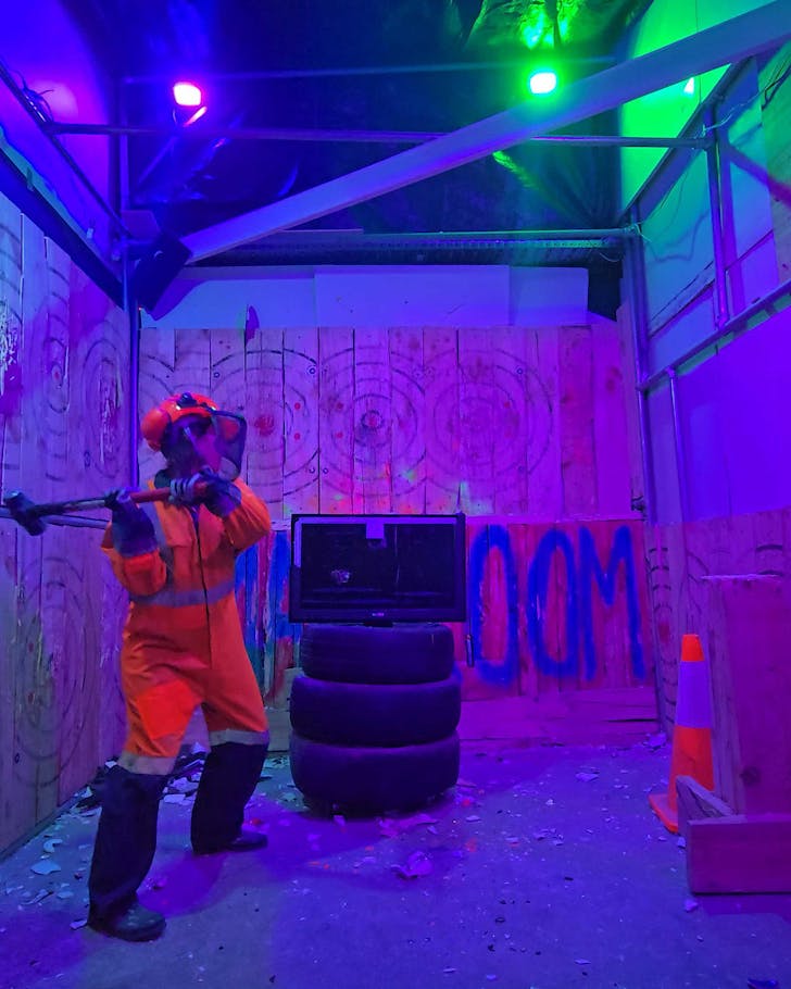Alice, dressed in PPE gear, prepares to slay a television with a large mallet.