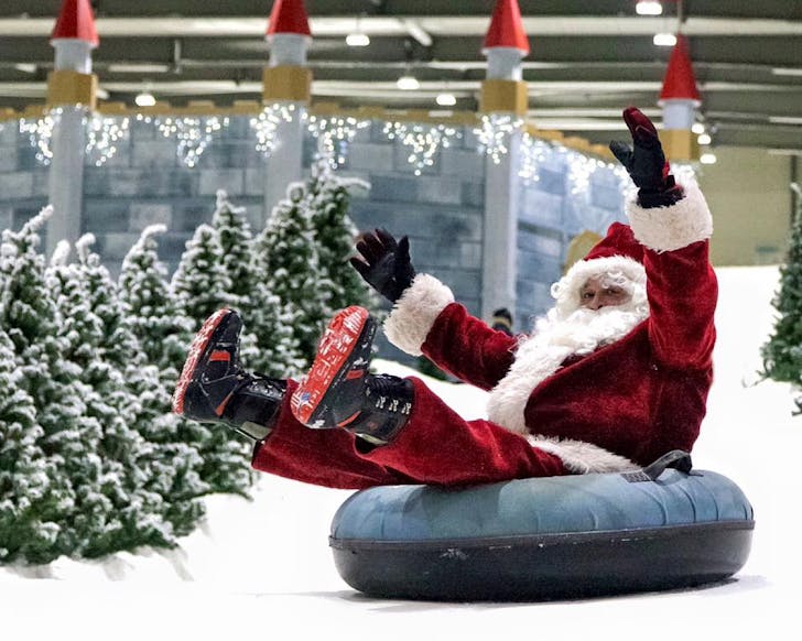 Santa rides a rubber ring down a snow slope.