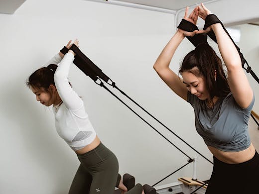 Two women using the arm straps on pilates reformer machines. 